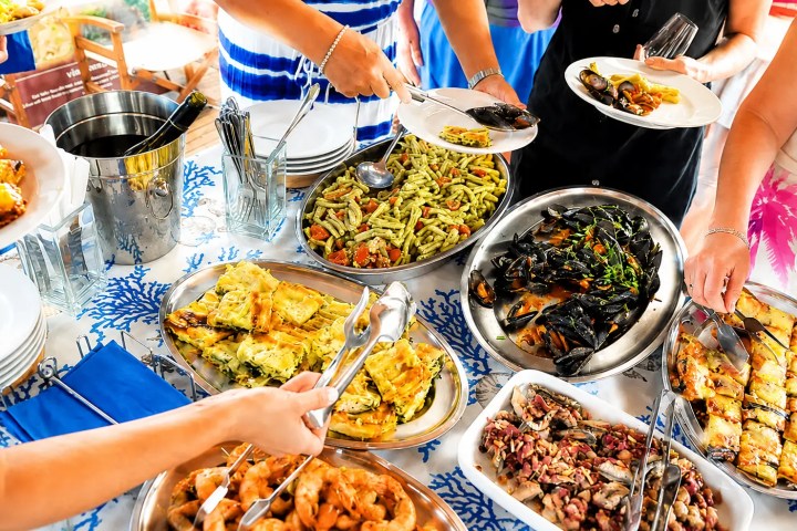 People serving food from a buffet with pasta and seafood.