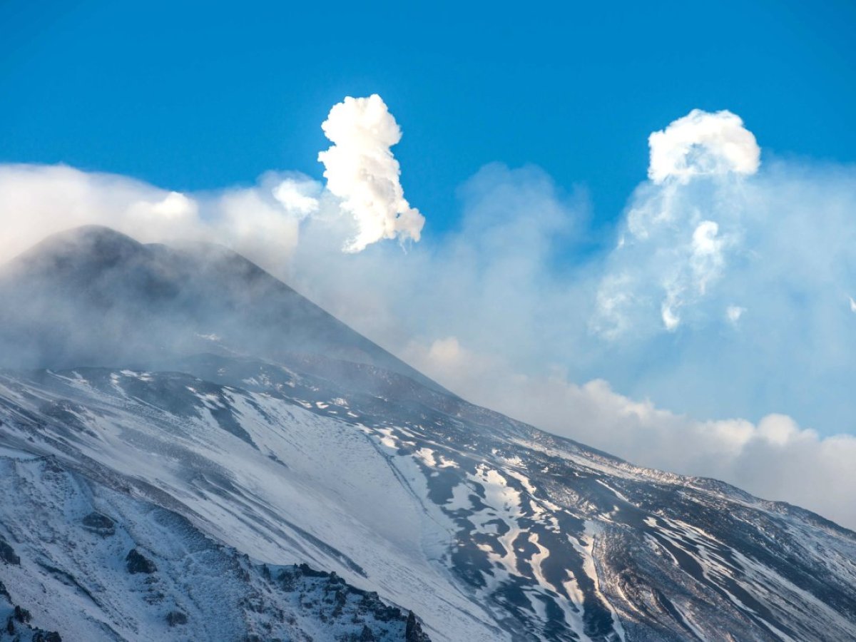 a group of clouds in the sky over a snow covered mountain