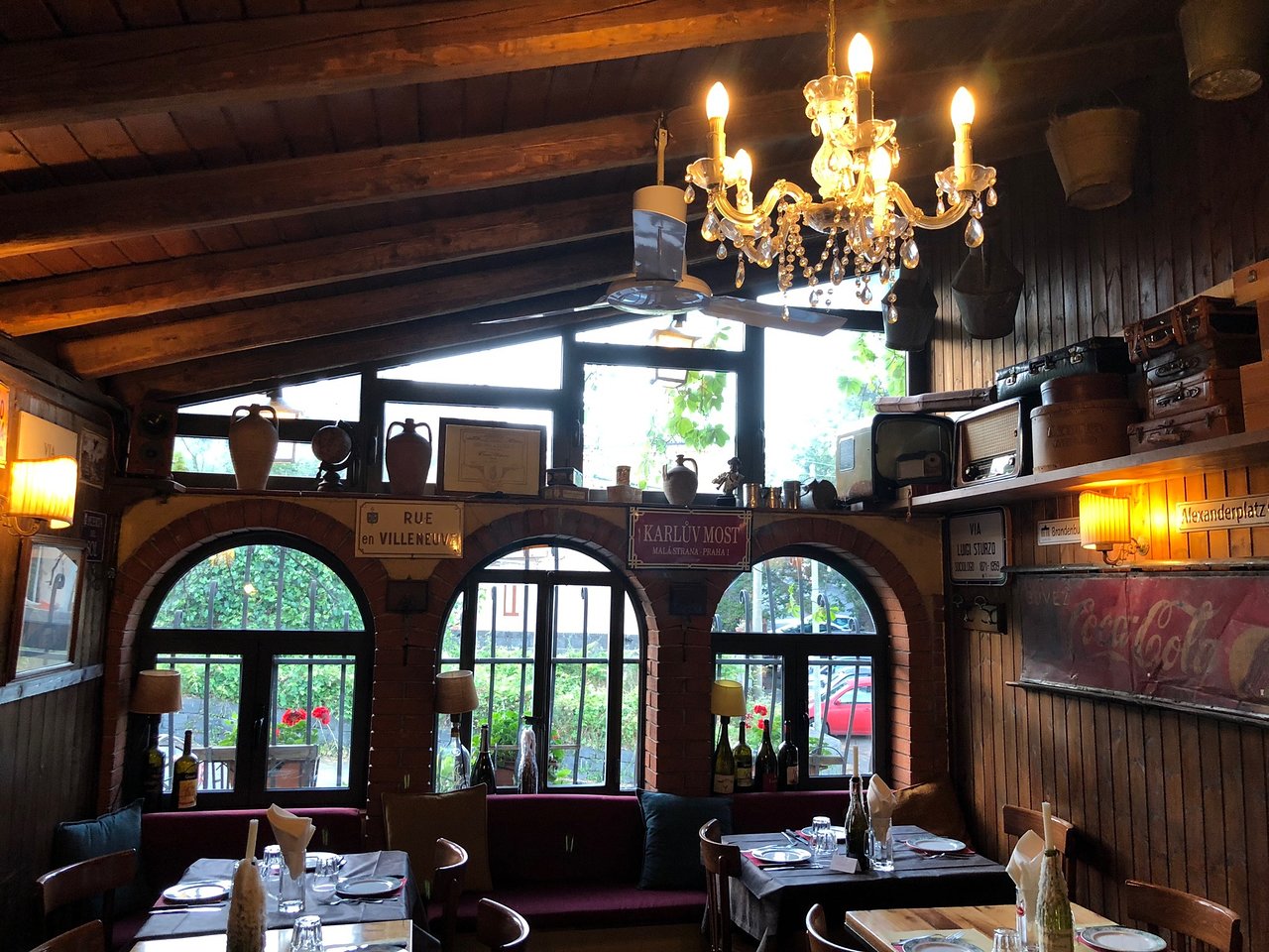 Cozy restaurant interior with wooden ceiling, chandelier, vintage decor, and set tables by arched windows.
