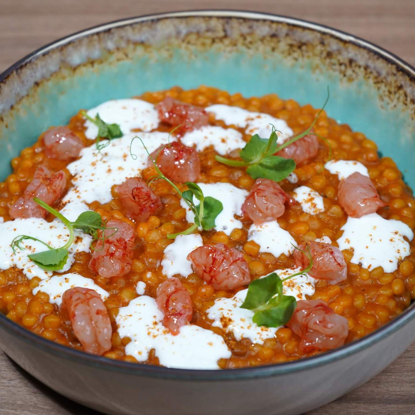 Colorful dish with couscous, creamy sauce, garnished with herbs and red pieces in a ceramic bowl.