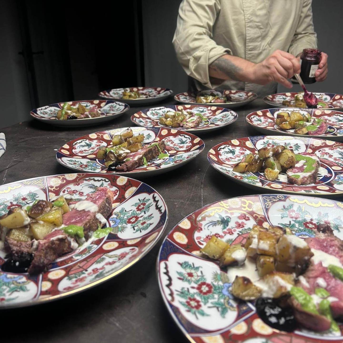 Chef garnishing plates with meat and roasted potatoes on colorful dishware.