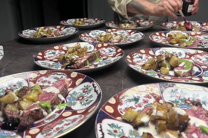 Chef garnishing plates with meat and roasted potatoes on colorful dishware.