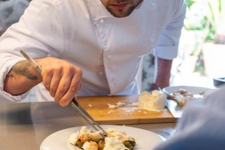 Chef plating a dish with tweezers while a person watches on in a kitchen.