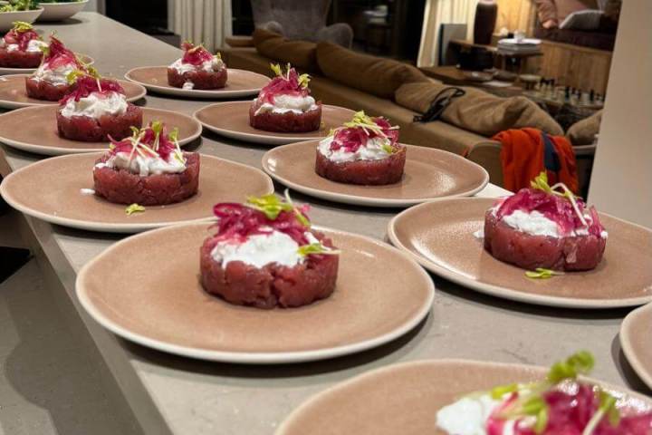 Plates of beef tartare with garnish on a counter in a modern living room.