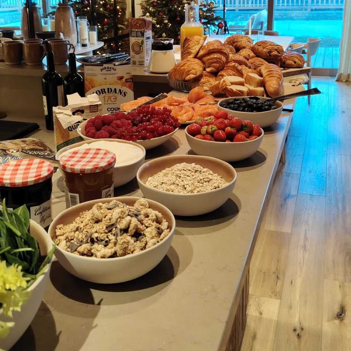Breakfast buffet with pastries, fruits, cereals, and a Christmas tree in the background.