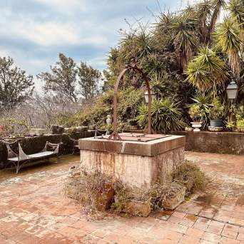 Old stone well on a tiled patio with benches and lush greenery.