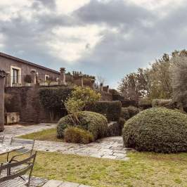 House with stone patio and neatly trimmed garden shrubs under a cloudy sky.