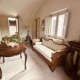 Vintage room with patterned couch, wooden table, plants, and open windows.