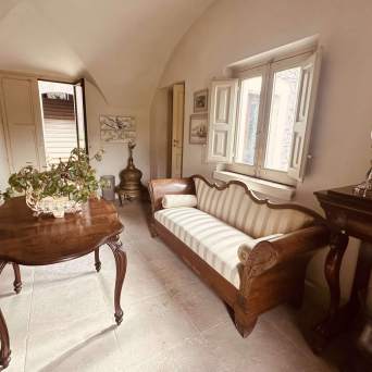 Vintage room with patterned couch, wooden table, plants, and open windows.