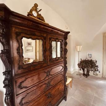 Room with antique wooden dresser, ornate mirrors, clock on top, plant, and lamp nearby.
