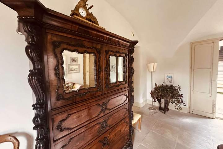 Room with antique wooden dresser, ornate mirrors, clock on top, plant, and lamp nearby.