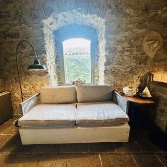 Cozy stone room with a sofa, window, floor lamp, and wooden side table with decor.