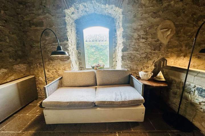 Cozy stone room with a sofa, window, floor lamp, and wooden side table with decor.
