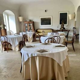 Elegant dining room with round tables, white tablecloths, and wooden chairs, decorated with artwork and sculptures.