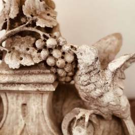 Vintage sculpture of bird with grapes and leaves in sepia tone.