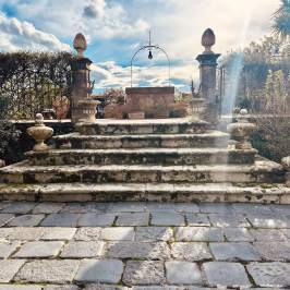 Stone steps with ornate balustrades leading to an old well under a cloudy sky.
