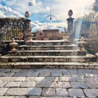 Stone steps with ornate balustrades leading to an old well under a cloudy sky.