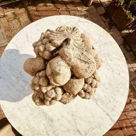 Stone fruit sculpture on round marble table, brick patio background.