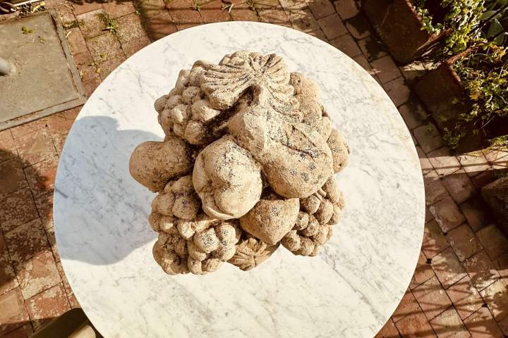 Stone fruit sculpture on round marble table, brick patio background.