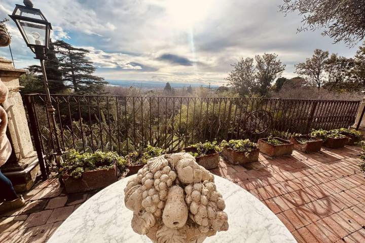Stone fruit sculpture on a table with a scenic terrace view of trees and sky.