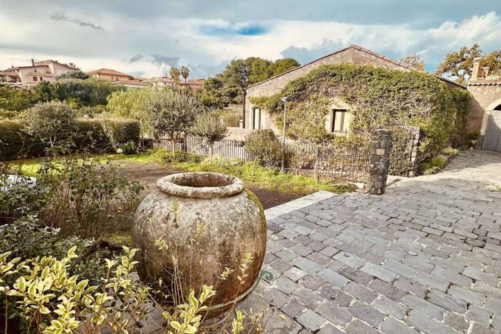 Stone path and large pot with rustic house and cloudy sky in background