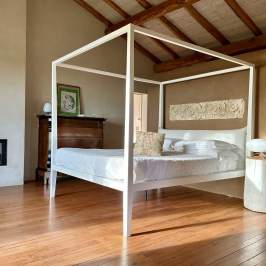 Modern bedroom with four-poster bed, wooden floor, and wall art.