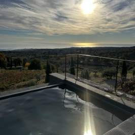 Sunset view of landscape and water reflecting sunlight, with hills in background and cloudy sky.