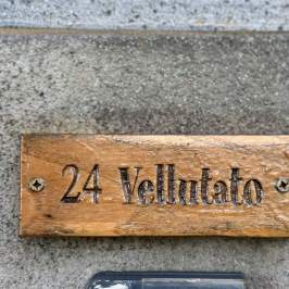Wooden sign with '24 Vellutato' engraved, attached to a concrete wall.