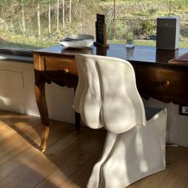 Modern chair with curvy design at a wooden desk by a large window with a view of a grassy field.