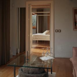 Room with glass table, doorway view to bed with white linens and curtains.