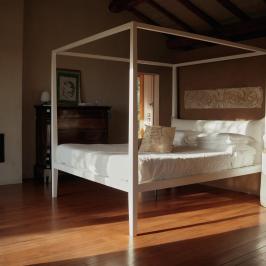 A minimalist bedroom with a four-poster bed, wood floors, and a modern fireplace.