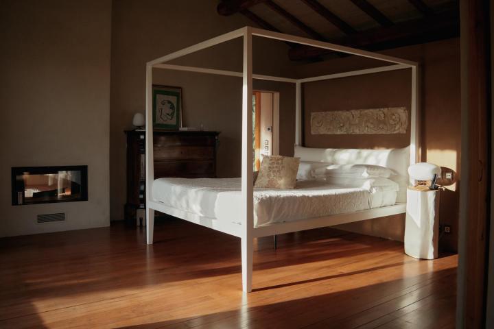 A minimalist bedroom with a four-poster bed, wood floors, and a modern fireplace.