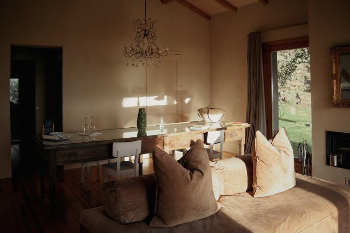 Cozy room with chandelier, wooden table, sofa, and window view of garden.