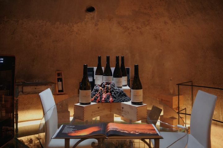 Wine bottles on wooden crates with grapes and open book on a round glass table.