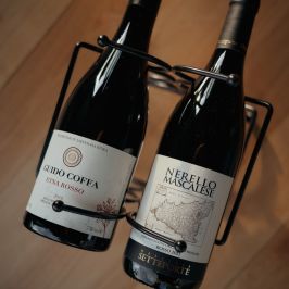 Two wine bottles in a metal rack on a wooden floor.