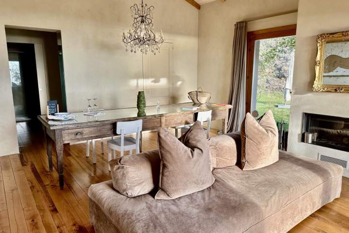 Cozy living room with tan sofa, wooden table, chandelier, and large window with view of garden.