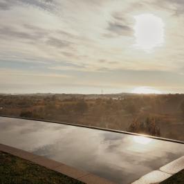 Infinity pool with scenic landscape and glowing sun in the sky.