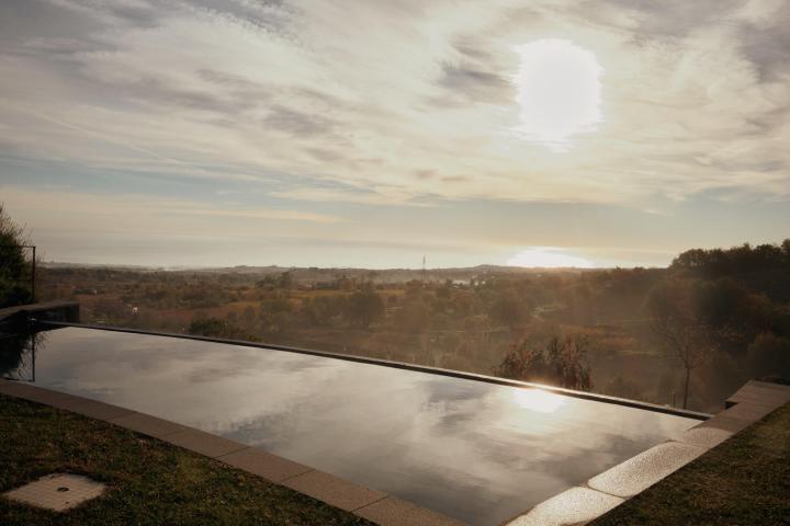 Infinity pool with scenic landscape and glowing sun in the sky.