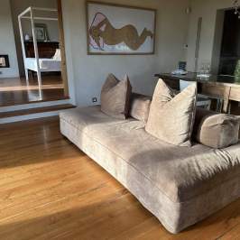Open living area with brown couch, wooden table, art, and steps leading to a bedroom.
