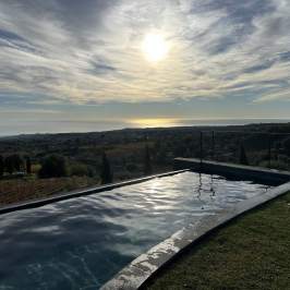 Infinity pool overlooking a scenic landscape with a setting sun and cloudy sky.