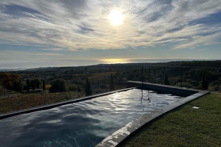 Infinity pool overlooking a scenic landscape with a setting sun and cloudy sky.