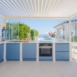 Modern outdoor kitchen with blue cabinets, glass walls, and ocean view.