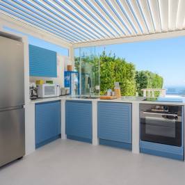 Modern outdoor kitchen with blue cabinets, stainless steel appliances, and ocean view.