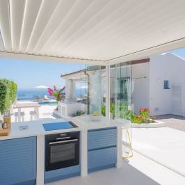 Outdoor kitchen with ocean view, blue cabinets, and a white countertop under a pergola.