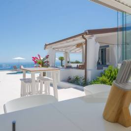 Modern kitchen view of a sunny patio with pool and sea in the background.