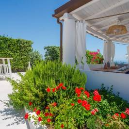 Outdoor patio with white pergola, red flowers, and sea view.