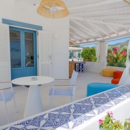 White terrace with blue door, chairs, table, ottomans, and plants.