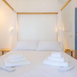 Minimalist bedroom with canopy bed, white linens, folded towels, and blue door.