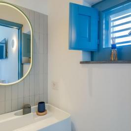 Bathroom with oval mirror, blue window, sink, and reed diffuser.