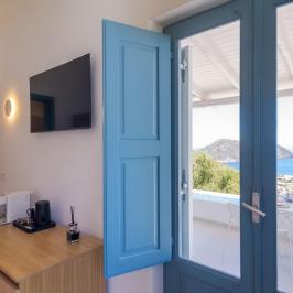 Room with blue door, TV, coffee maker, and sea view through open door.